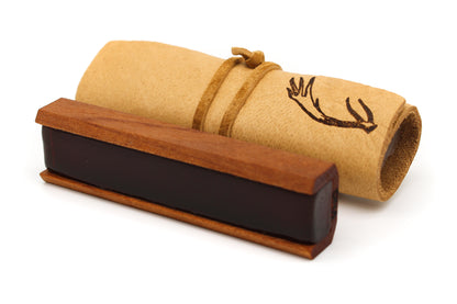 A dark rectangular cello rosin rests beside a rolled-up parchment tied with leather against a white background.