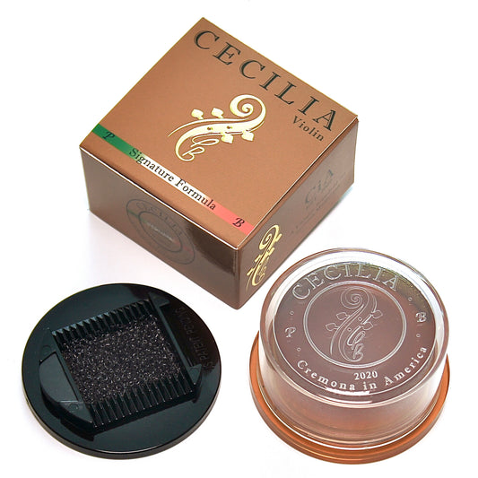 A round container of rosin sits beside its box; both are brown and display the "CECILIA Violin" logo.  A small, black applicator with a sponge is also present.  The box has the additional text "Signature Formula".