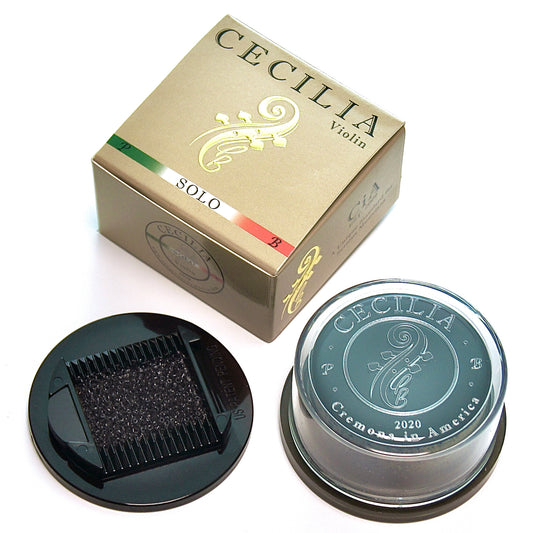 Violin rosin, contained in a clear plastic container with a black base, sits next to its gold and green box.  The box is labeled "CECILIA Violin SOLO".