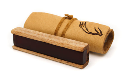 A dark rectangular viola rosin rests beside a rolled-up parchment tied with leather against a white background.