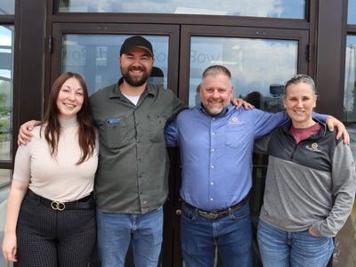 Four people posing together in front of a building with glass doors.